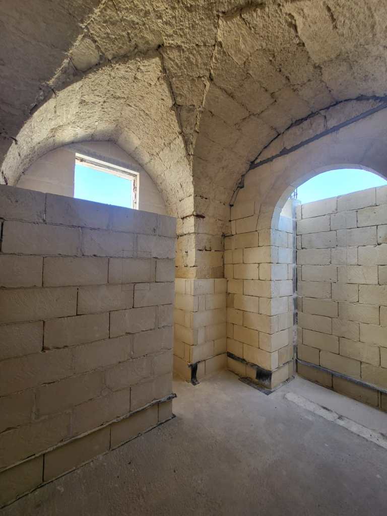 Interior view of a room with arched ceilings, featuring unfinished walls made of light-coloured blocks and a window providing natural light.